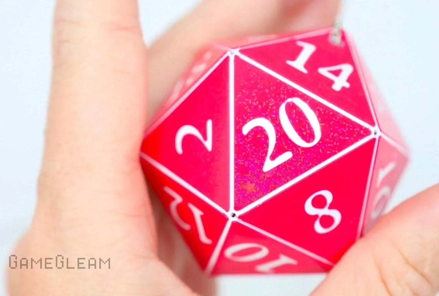 Hand holding a pink holographic 20-sided dice charm with white numbers