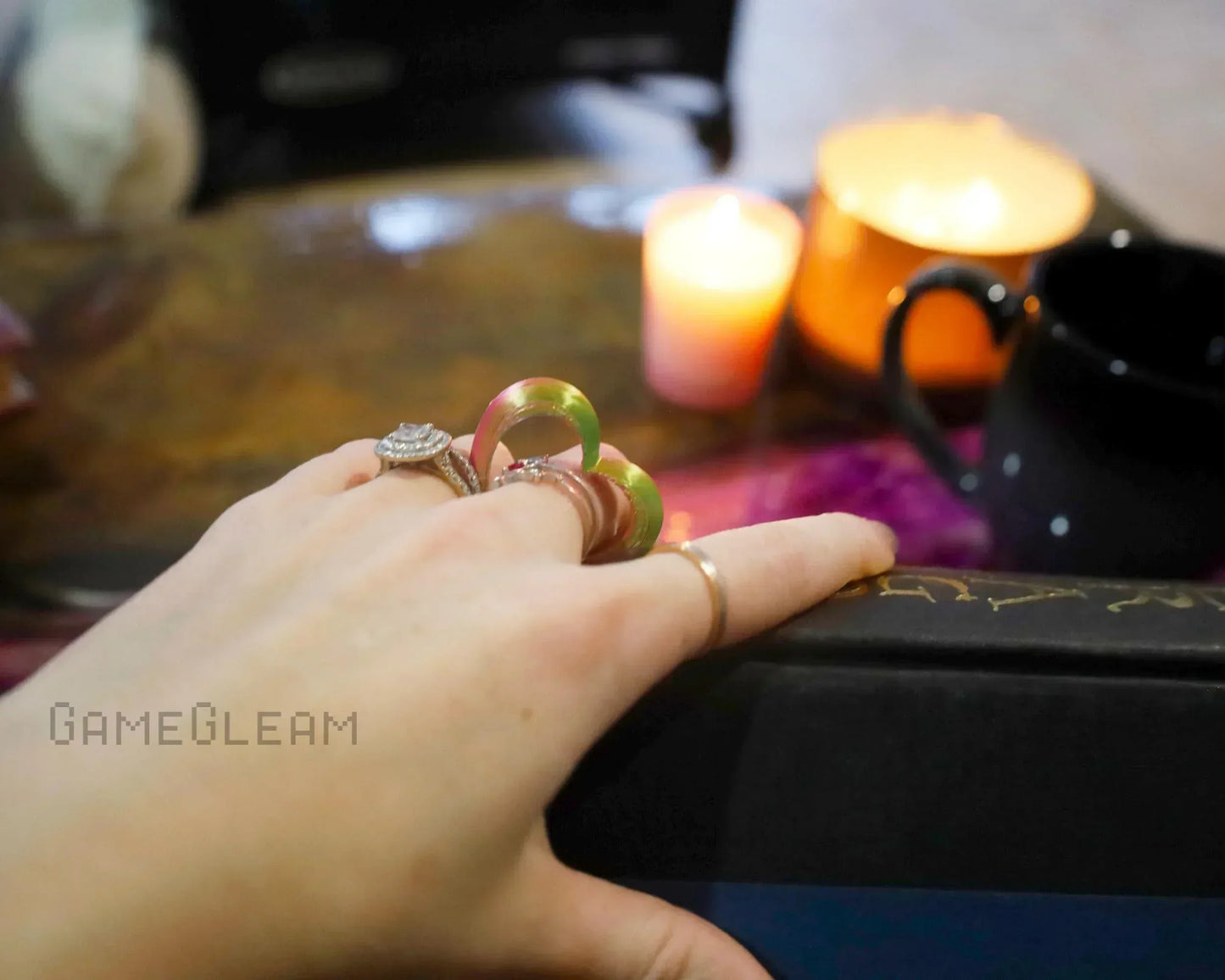 Hand with holographic dice charm ring, candles, and black mug on cozy table setup