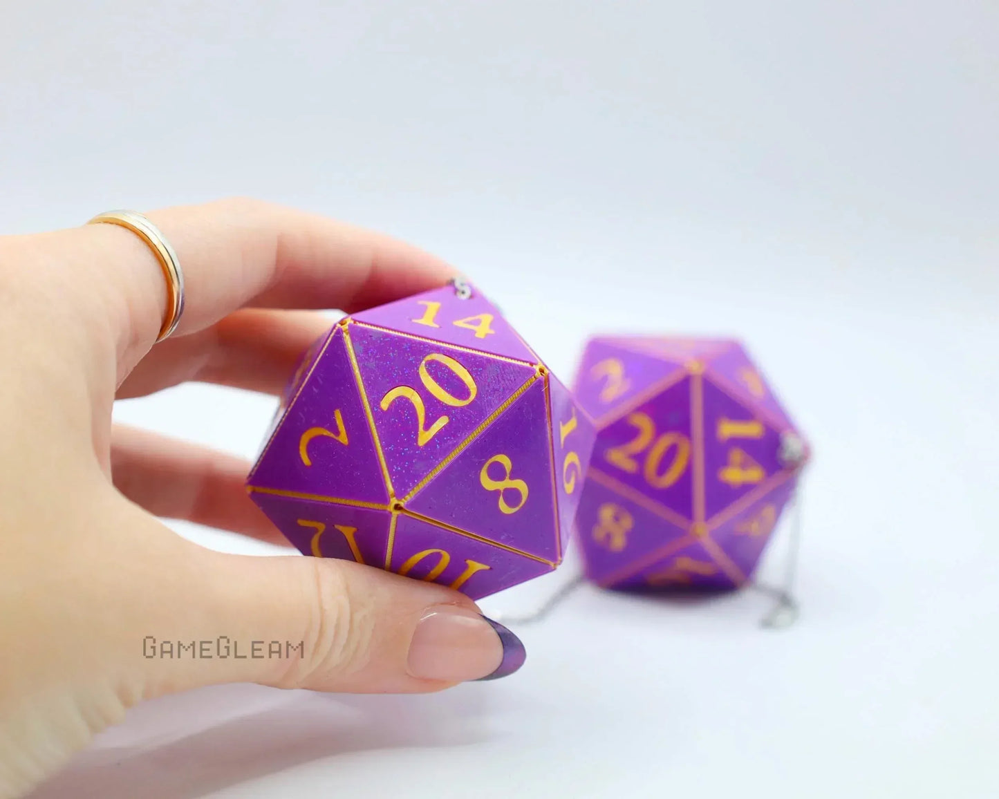 Hand holding purple twenty-sided dice charm with gold numbers, gamer car accessory