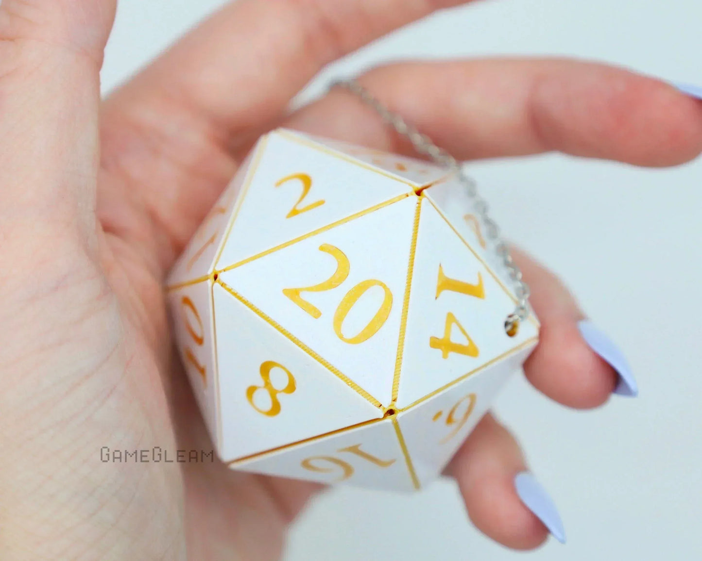 Hand holding a large white 20-sided dice charm with gold numbers and a silver chain