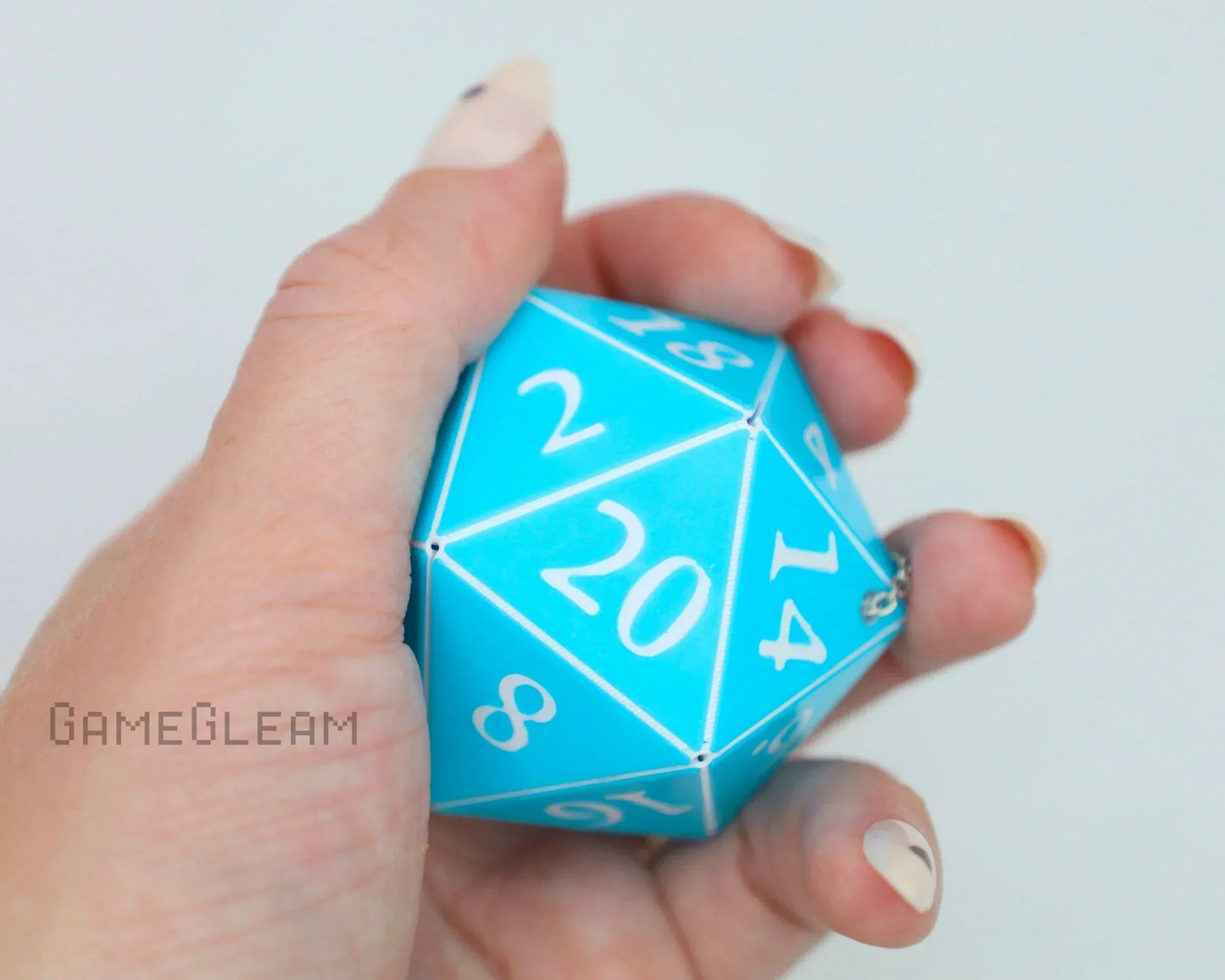 Hand holding a large turquoise 20-sided dice with white numbers, geek gift accessory