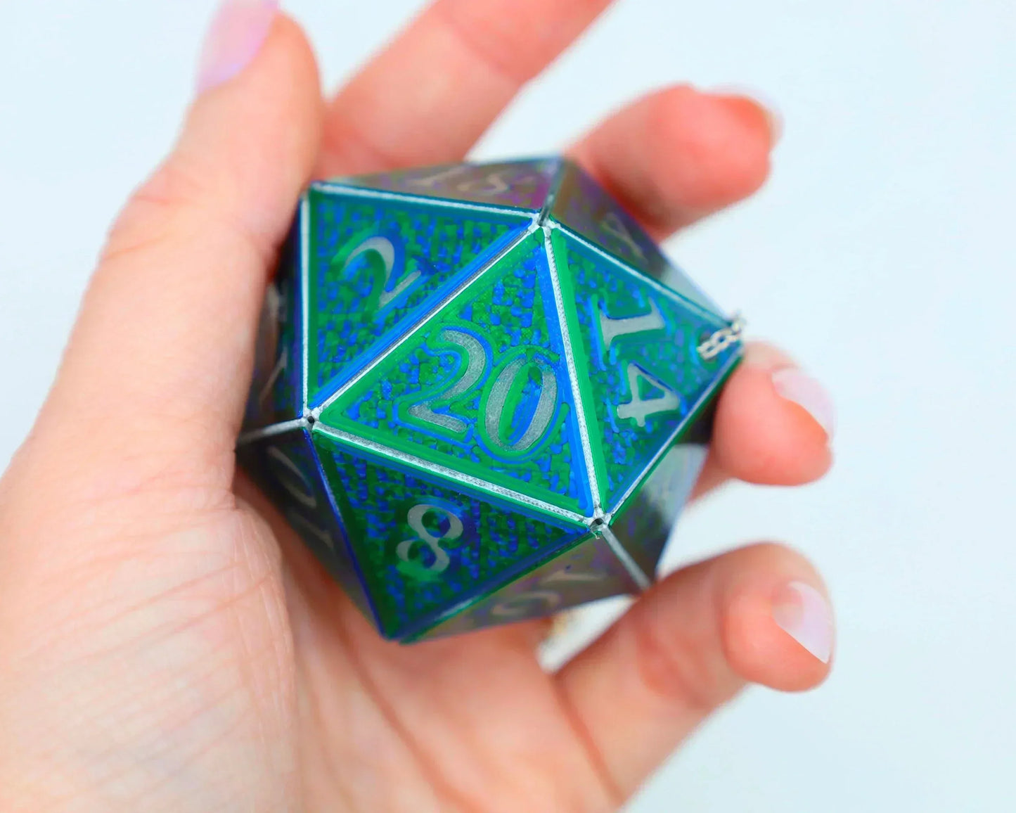 Hand holding a large holographic blue and green twenty-sided dice charm