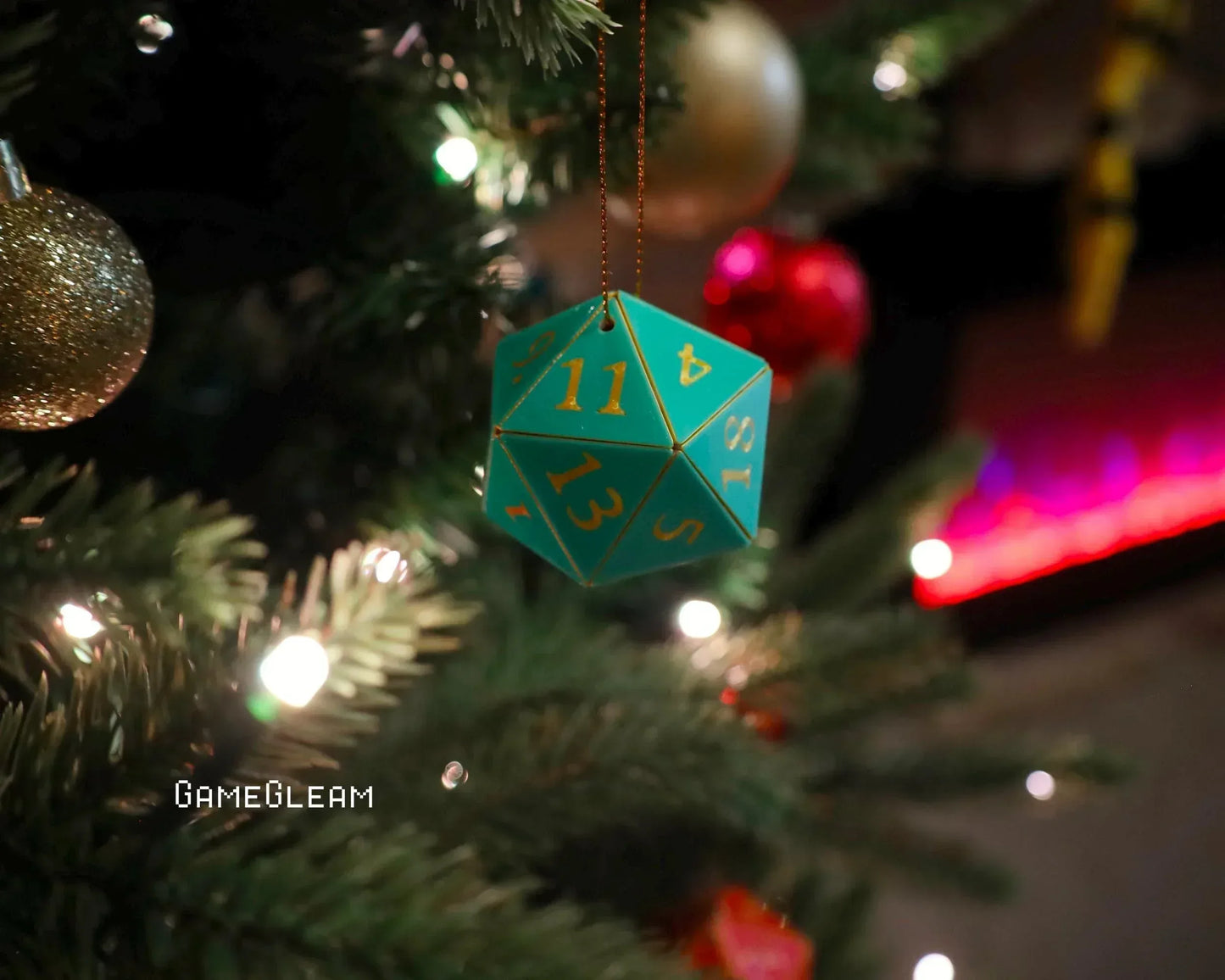 Green twenty-sided dice ornament with gold numbers hanging on holiday tree with lights.