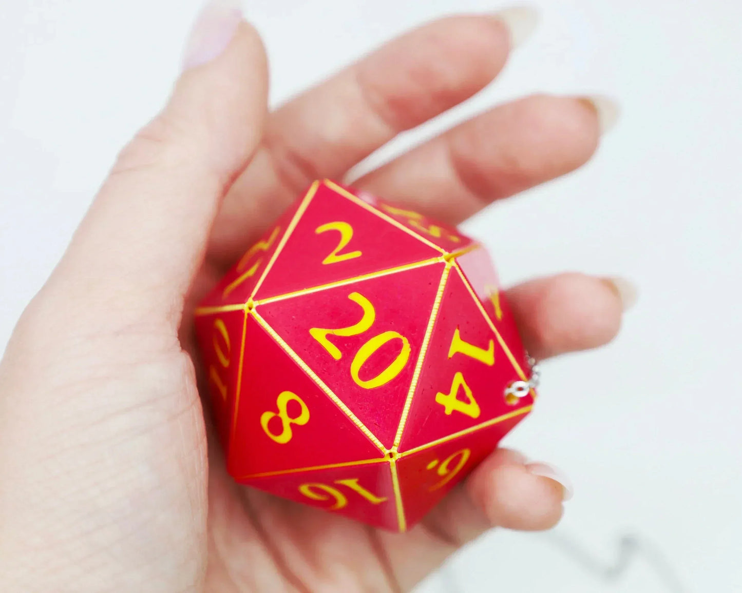 Hand holding a large red 20-sided dice with yellow numbers, gamer accessory closeup