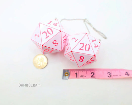 Pink twenty-sided dice car charm with chain, shown beside coin and measuring tape for scale