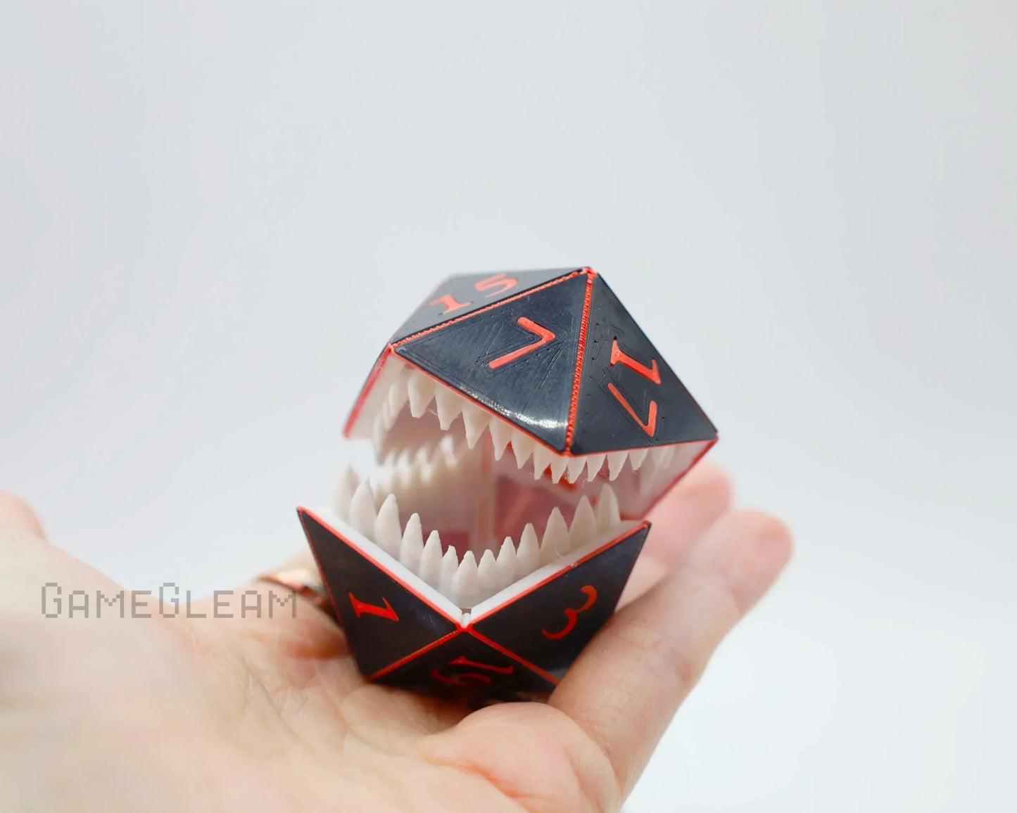 Hand holding a black and red polyhedral dice monster with sharp teeth, fantasy gamer gift