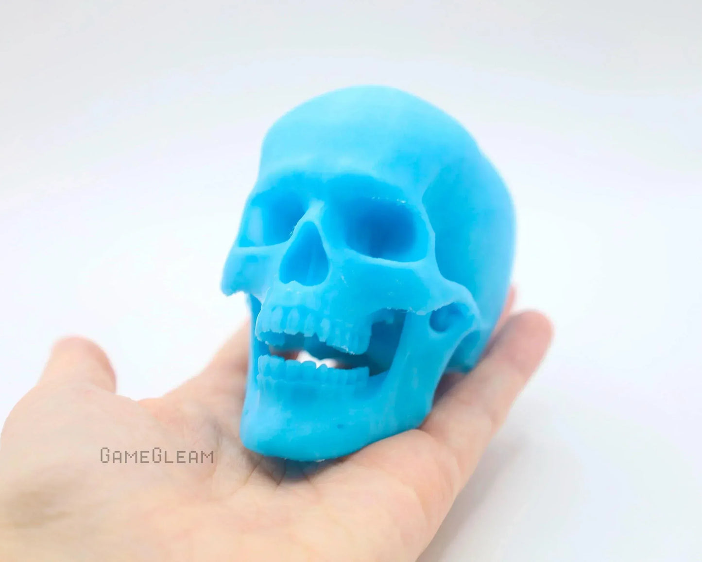 Hand holding a blue skull-shaped resin gamer accessory on a white background