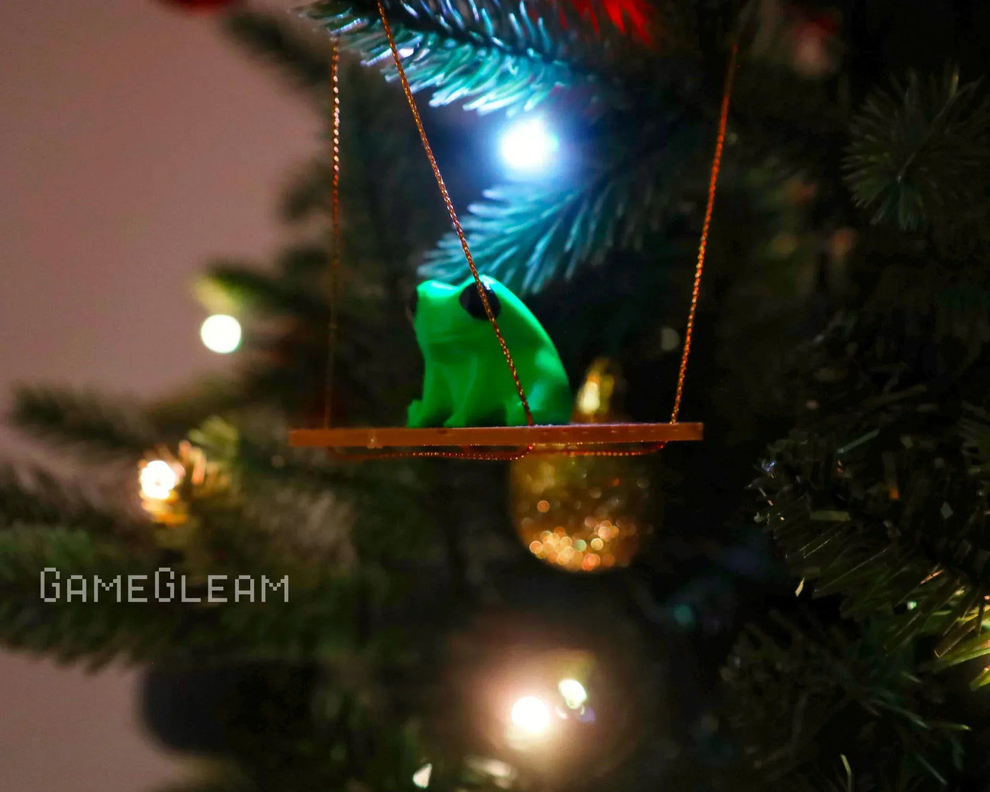 Green frog ornament on a wooden swing hanging on a lit Christmas tree branch
