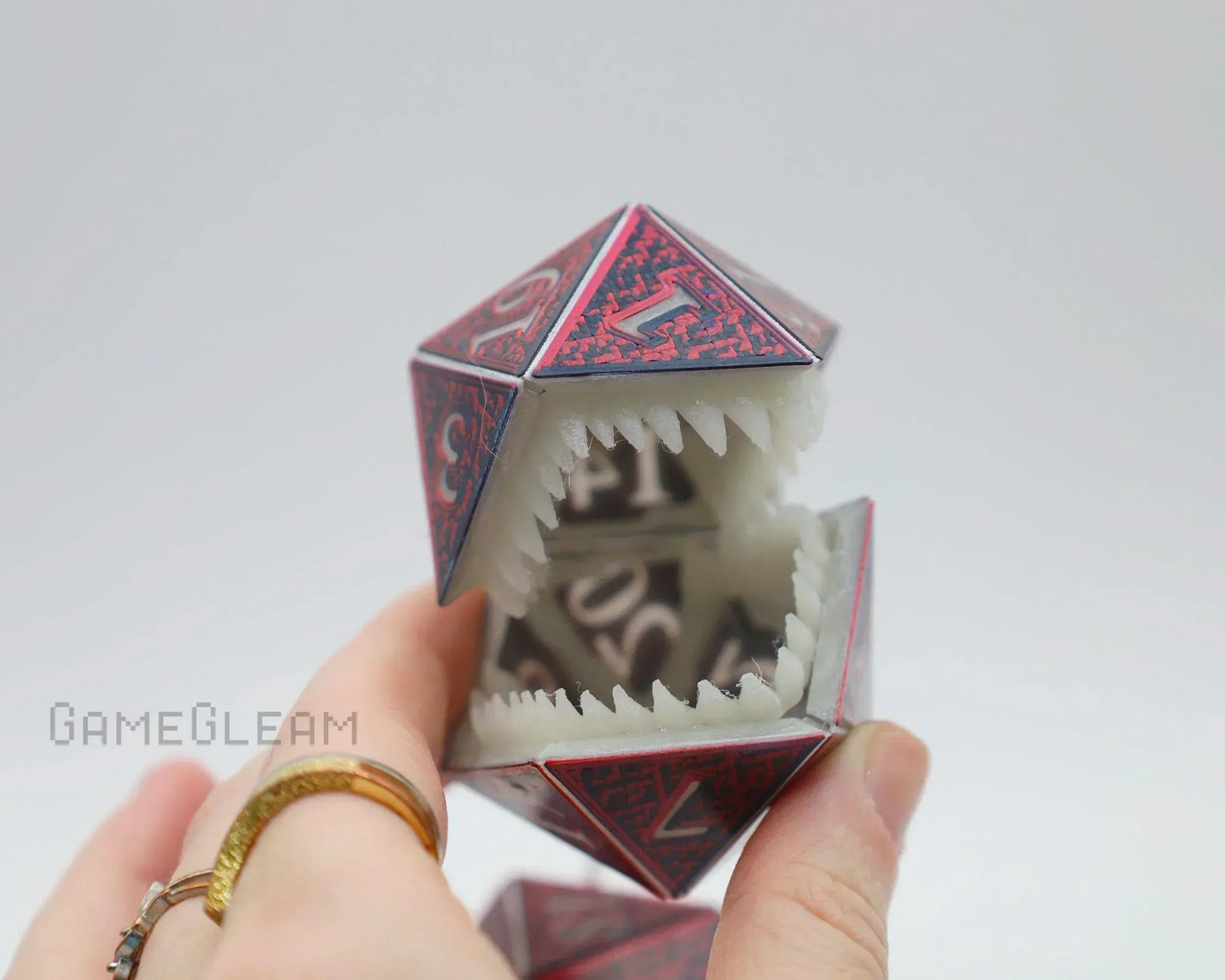 Hand holding a red polyhedral dice charm with white monster teeth, fantasy gaming accessory