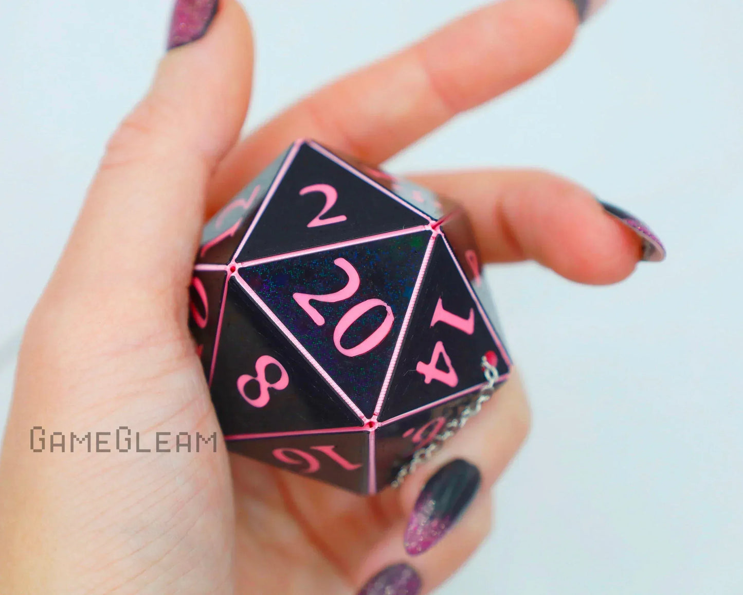 Hand holding a black and pink holographic large twenty-sided dice charm with chain.
