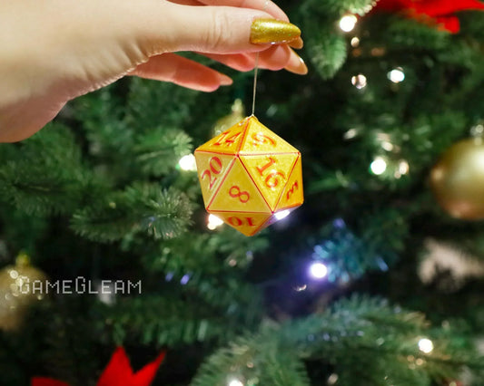 Hand holding a yellow and orange 20-sided dice ornament near a decorated Christmas tree