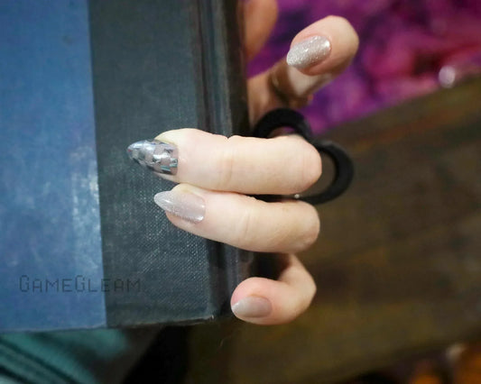 Hand with shimmery nude and metallic scale accent nails holding a black book