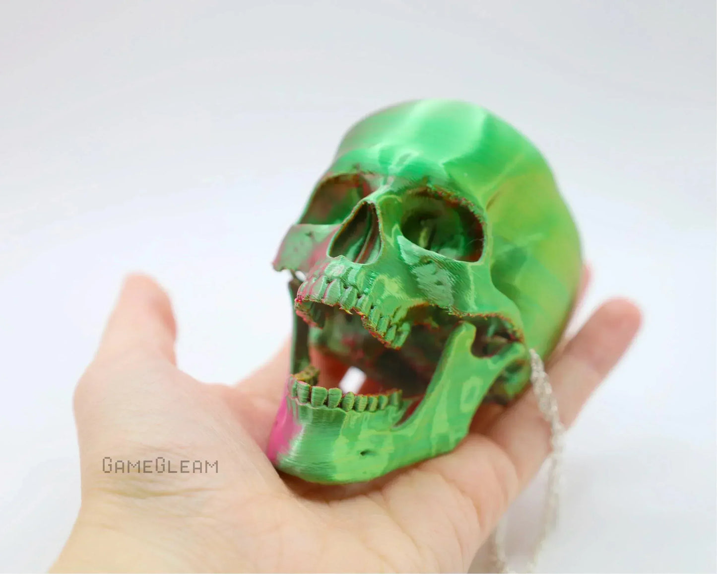 Hand holding a shiny green skull charm with silver chain, gamer gift accessory