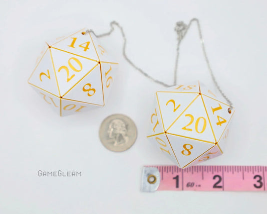White and gold 20-sided dice car charms with a chain, shown next to a ruler and a coin.
