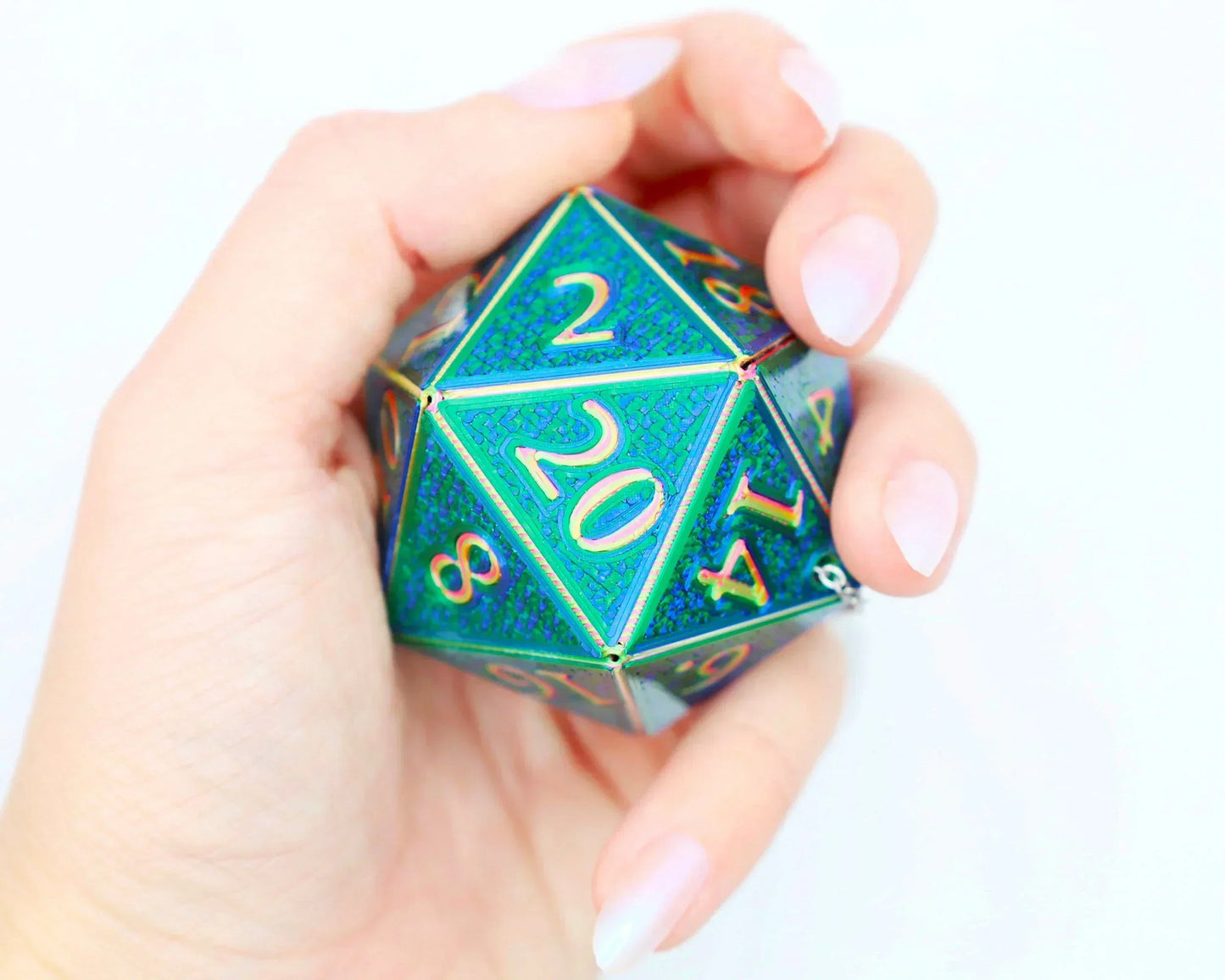 Hand holding a large holographic green and blue 20-sided dice charm for tabletop gaming.