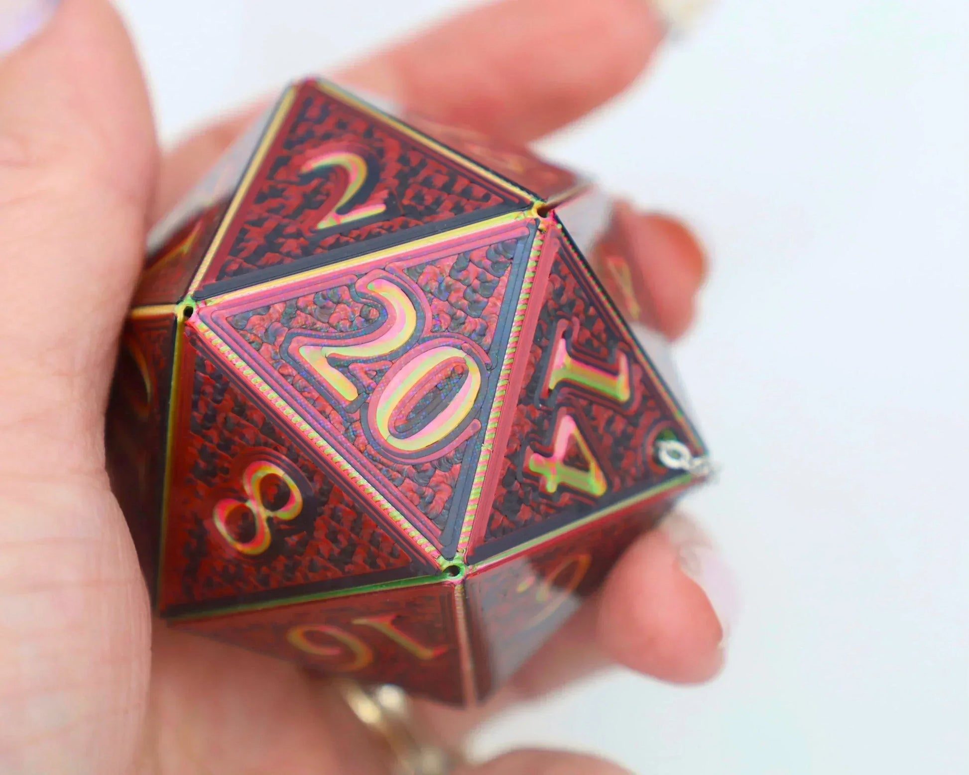 Hand holding a large holographic red metal twenty-sided dice charm for tabletop gaming.