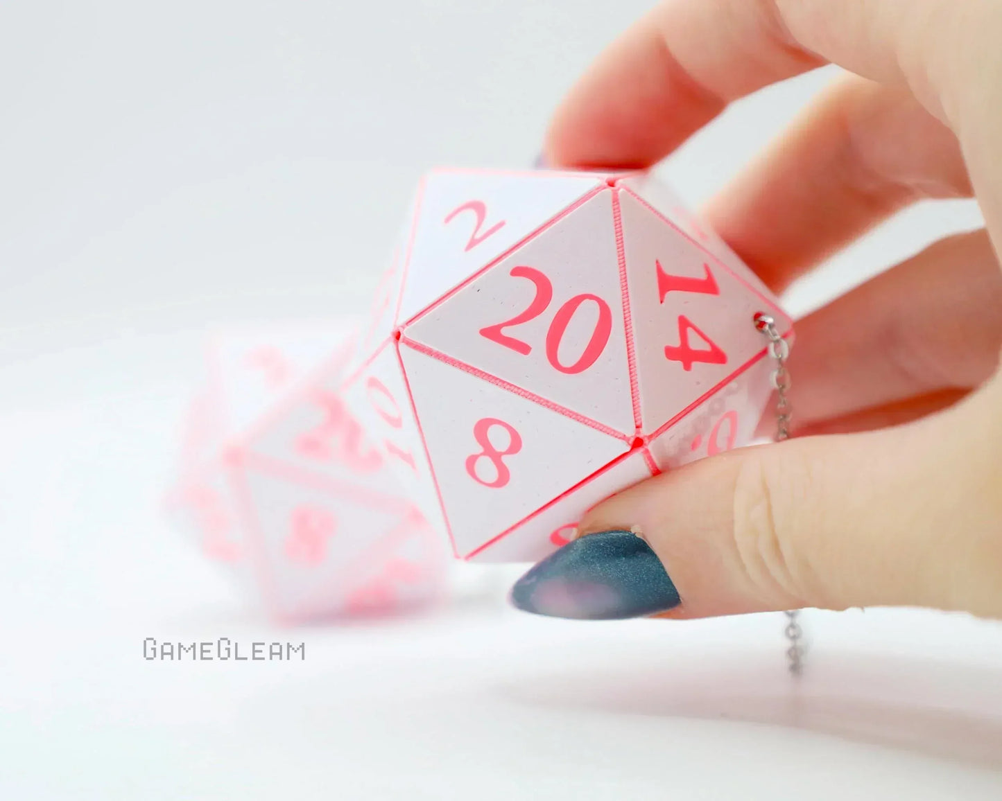 Hand holding pink and white twenty-sided dice car charm with chain, gamer gift accessory.
