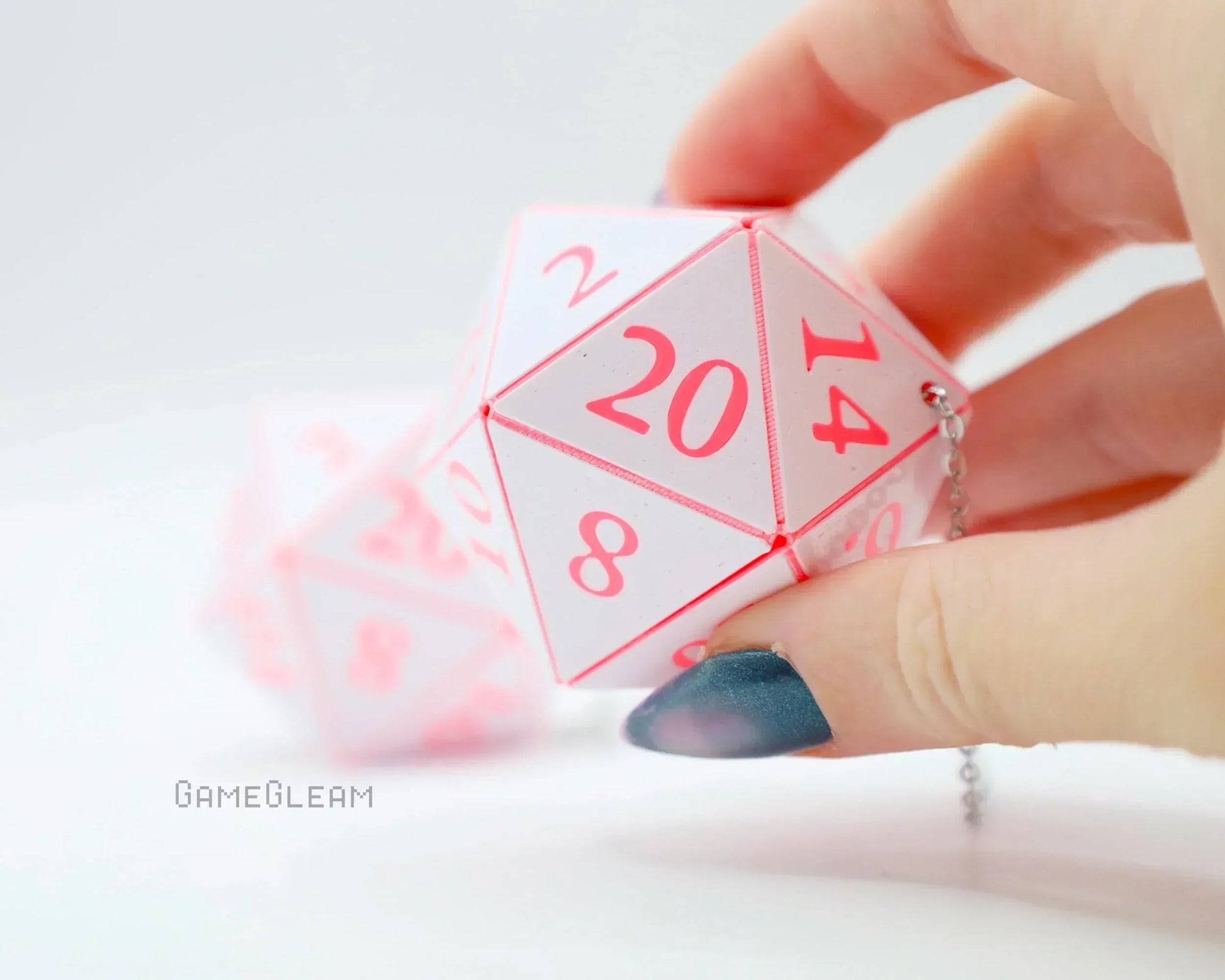 Hand holding pink and white twenty-sided dice car charm with chain, gamer gift accessory.