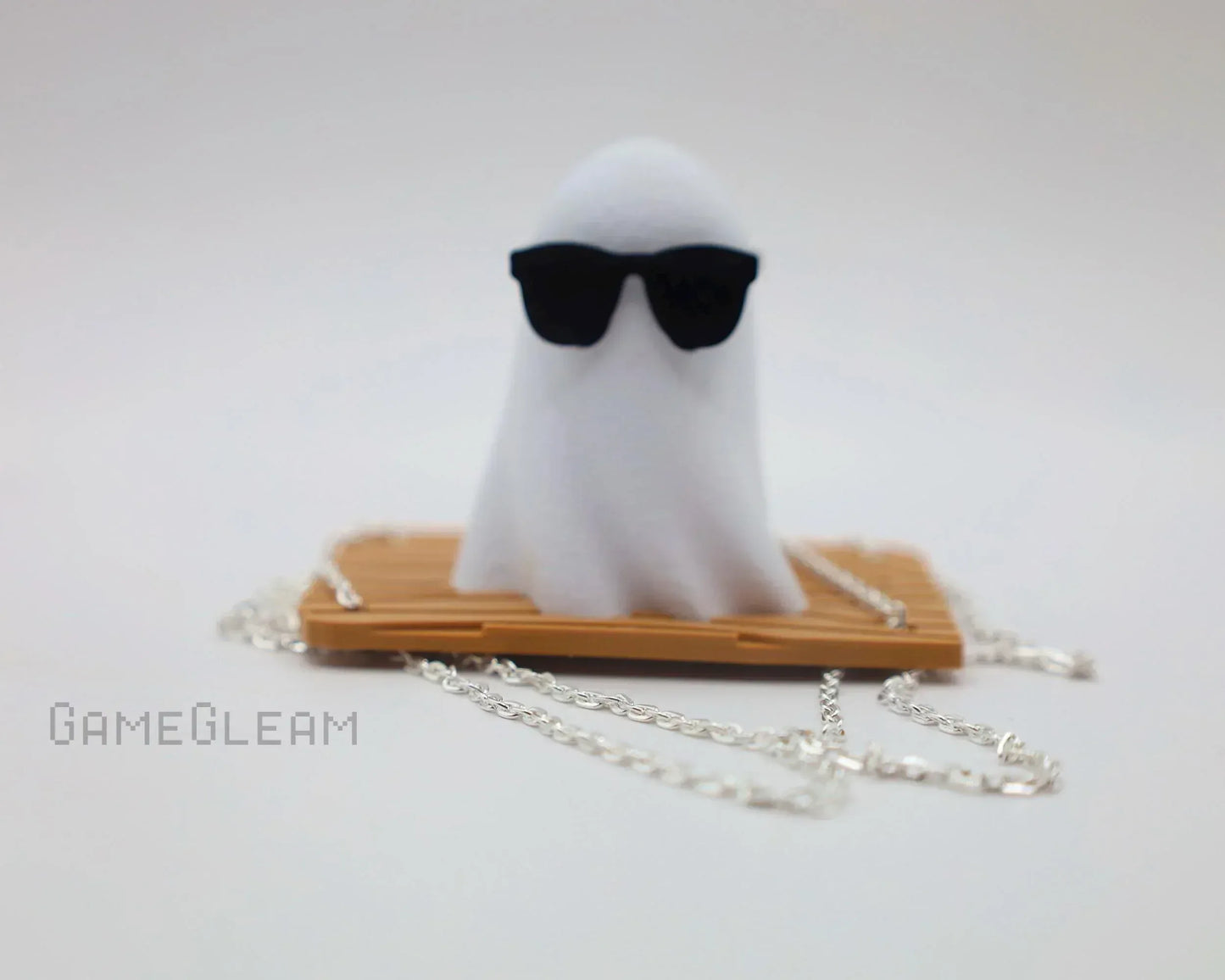 Handmade ghost figurine with sunglasses on a bamboo base, silver chain accessory, white background