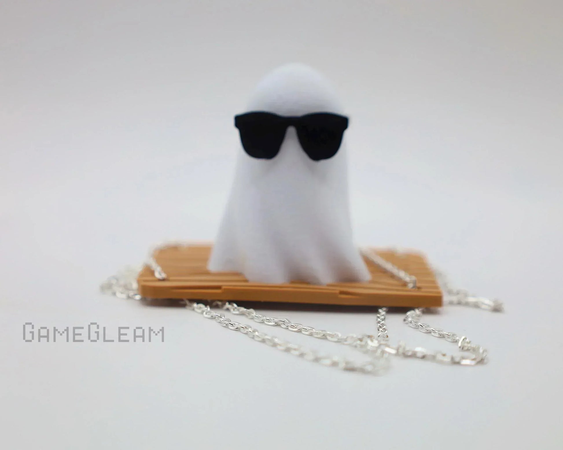 Handmade ghost figurine with sunglasses on a bamboo base, silver chain accessory, white background