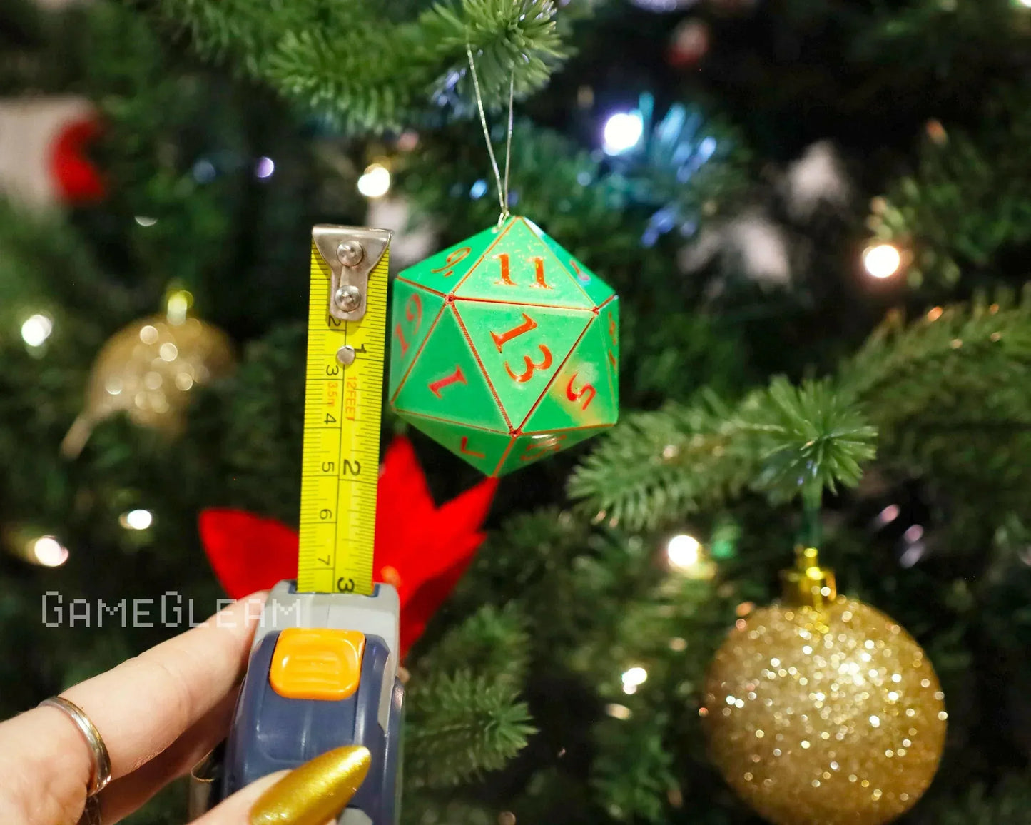 Green 20-sided dice ornament with red numbers hanging on a Christmas tree, measured for size.