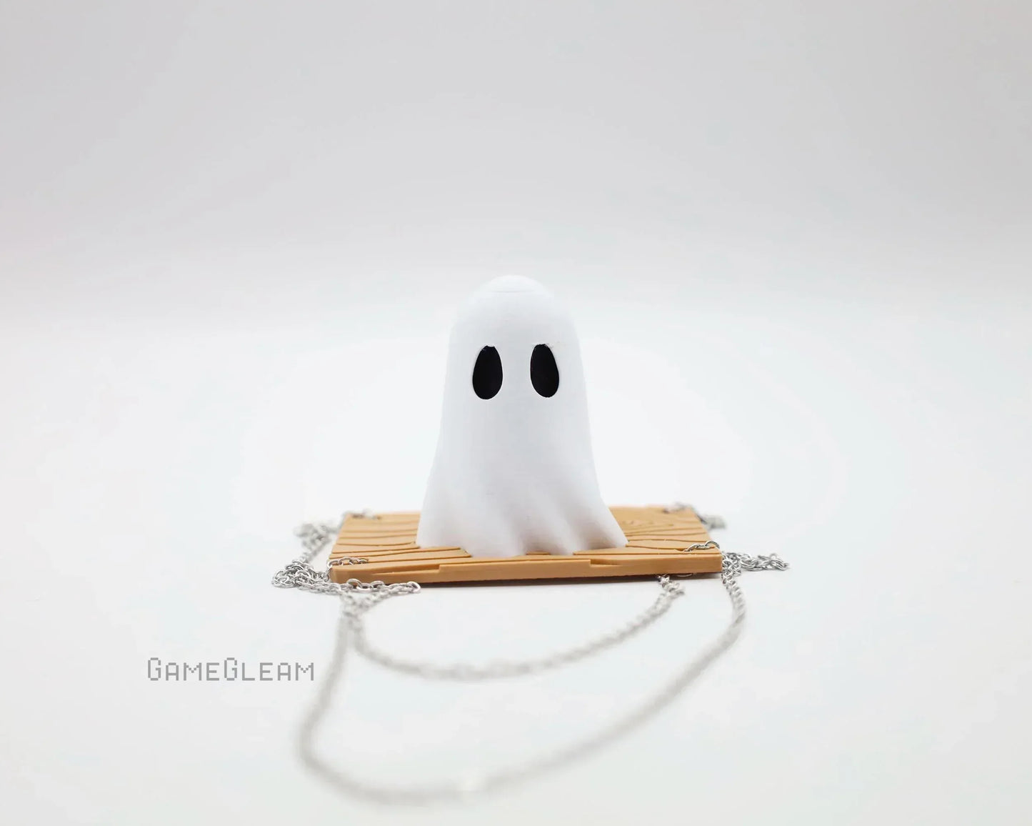 Cute handmade ghost figurine on a chain accessory with wooden plank base, minimalist style