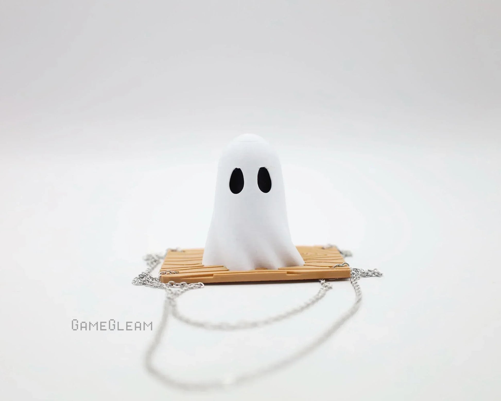 Cute handmade ghost figurine on a chain accessory with wooden plank base, minimalist style