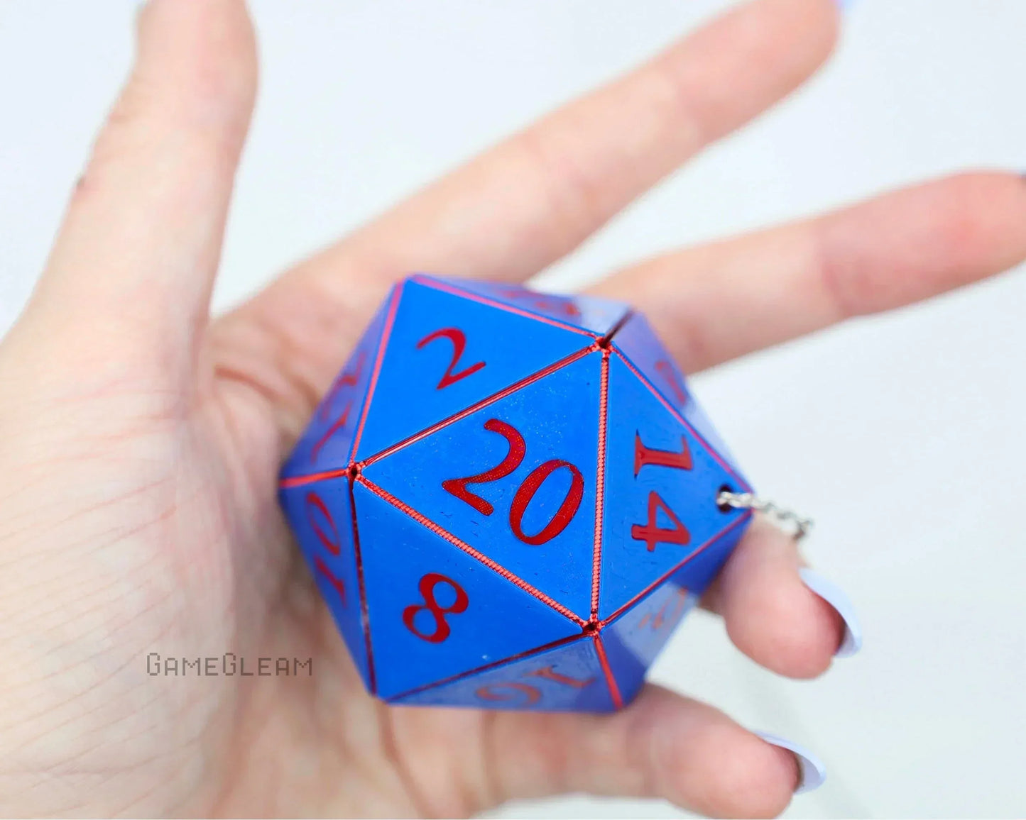 Hand holding a large blue twenty-sided dice car charm with red numbers and keychain clasp