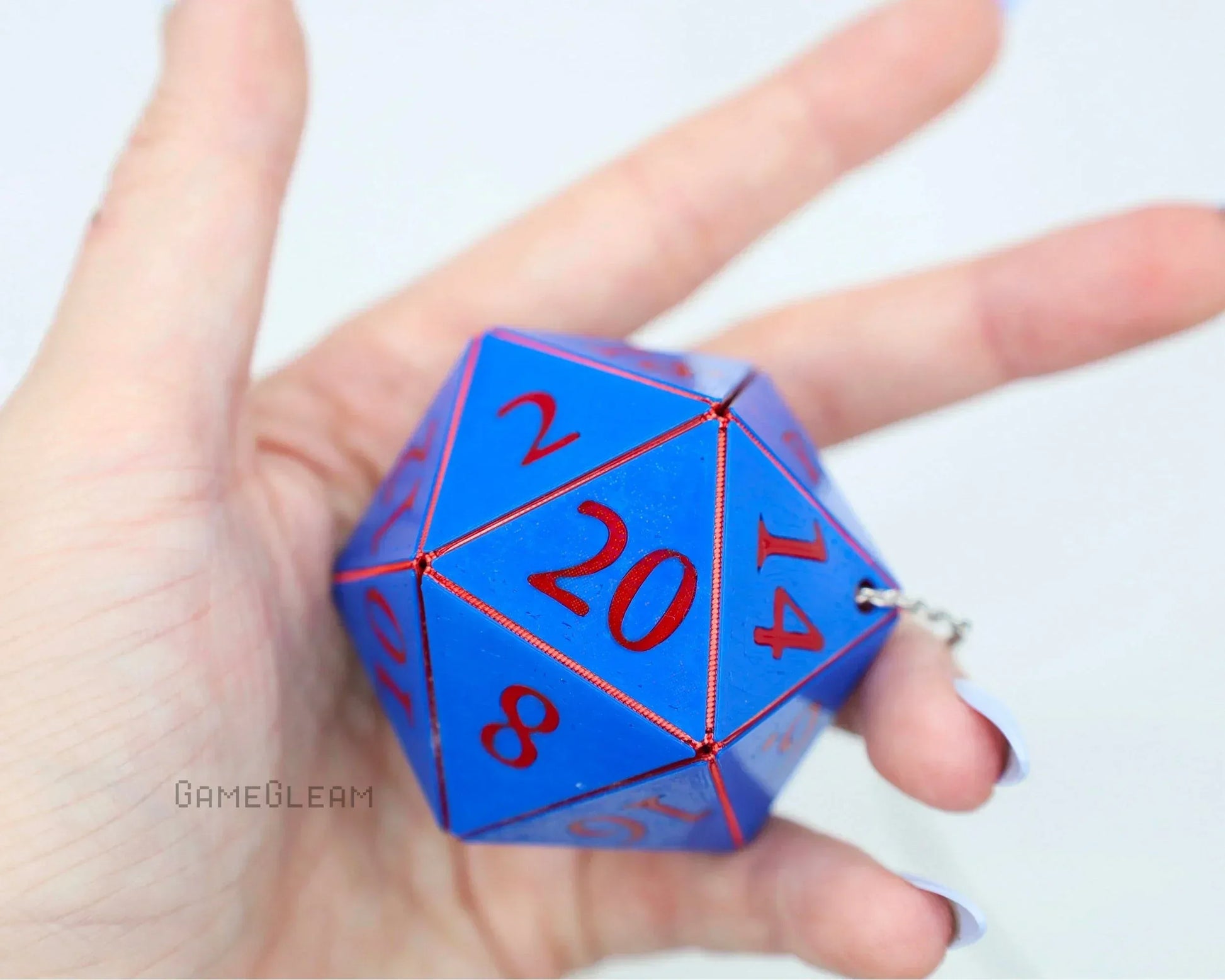 Hand holding a large blue twenty-sided dice car charm with red numbers and keychain clasp