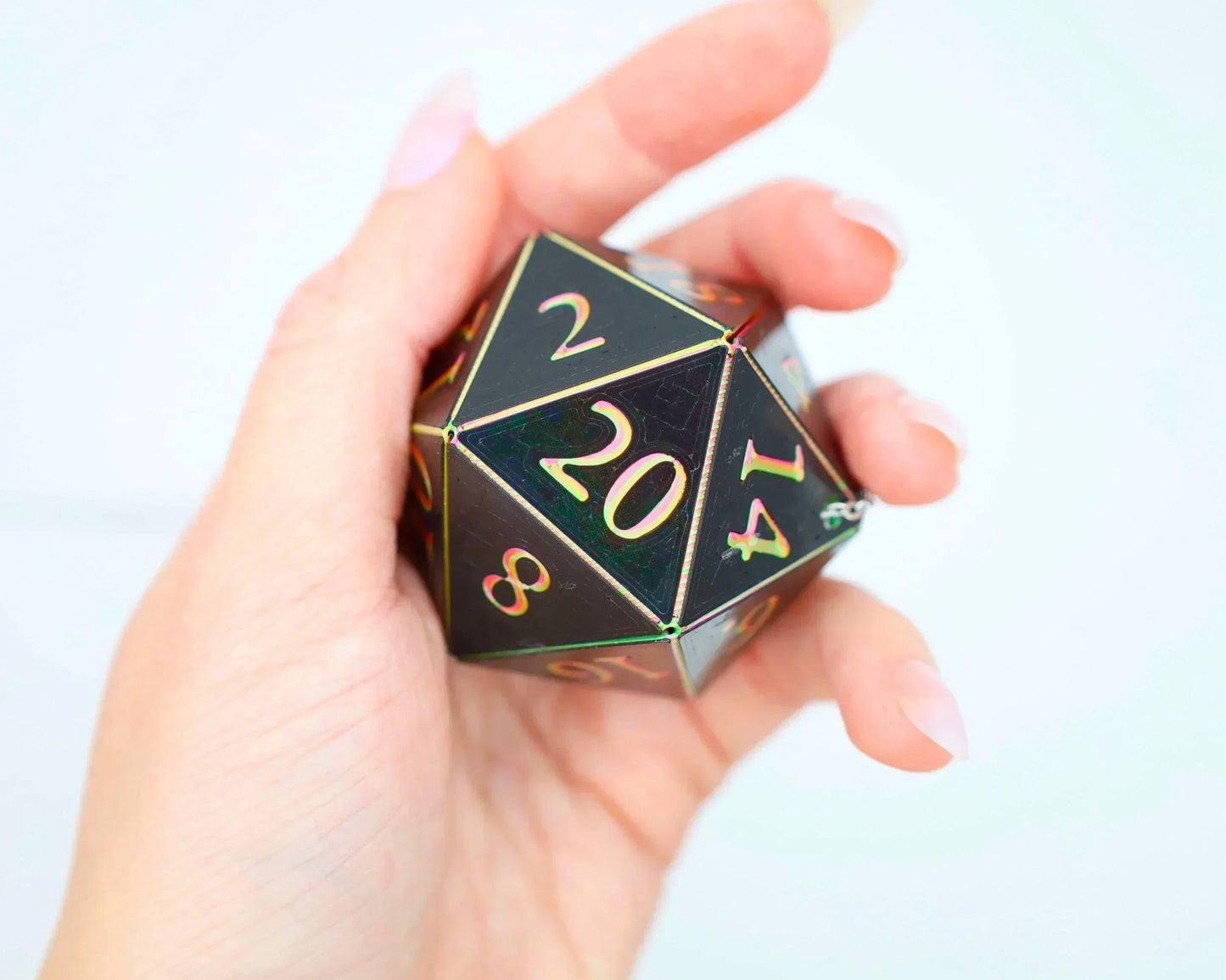 Hand holding a large holographic 20-sided dice charm with gold numbers for gamers