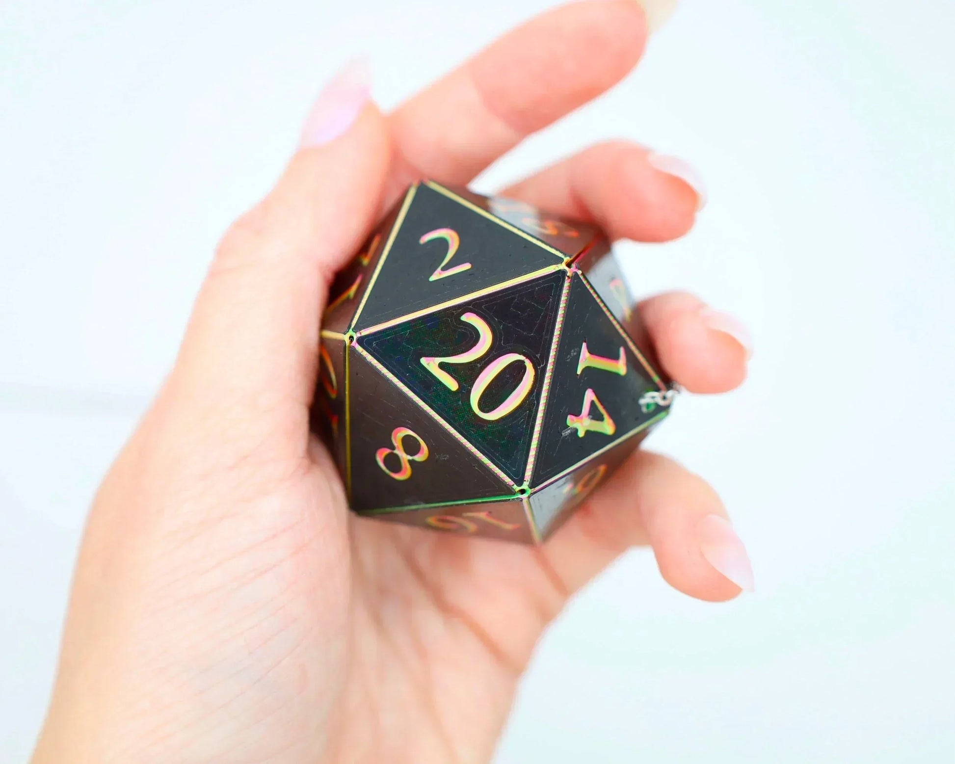 Hand holding a large holographic 20-sided dice charm with gold numbers for gamers