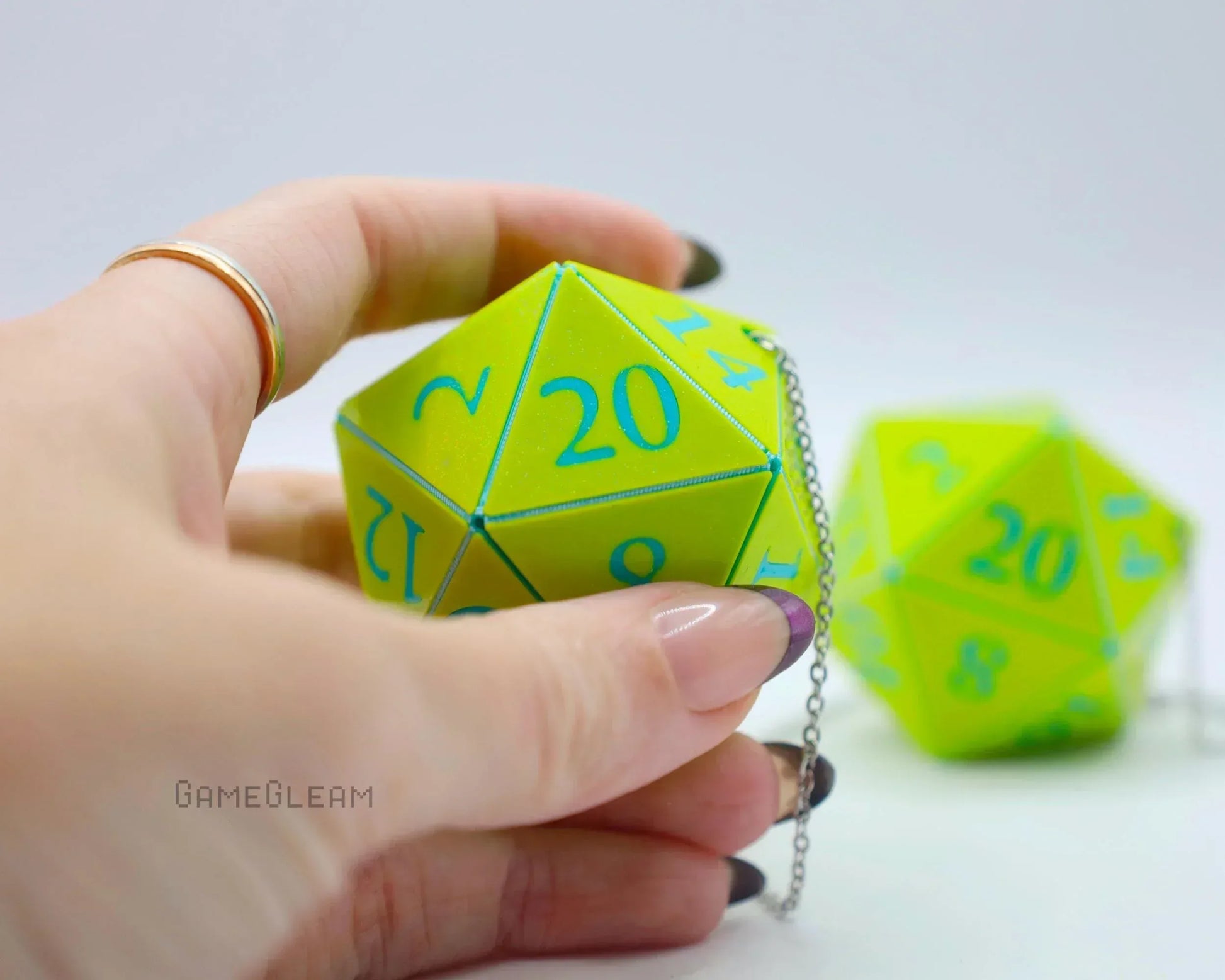 Hand holding a neon green twenty-sided dice car charm with blue numbers and chain.