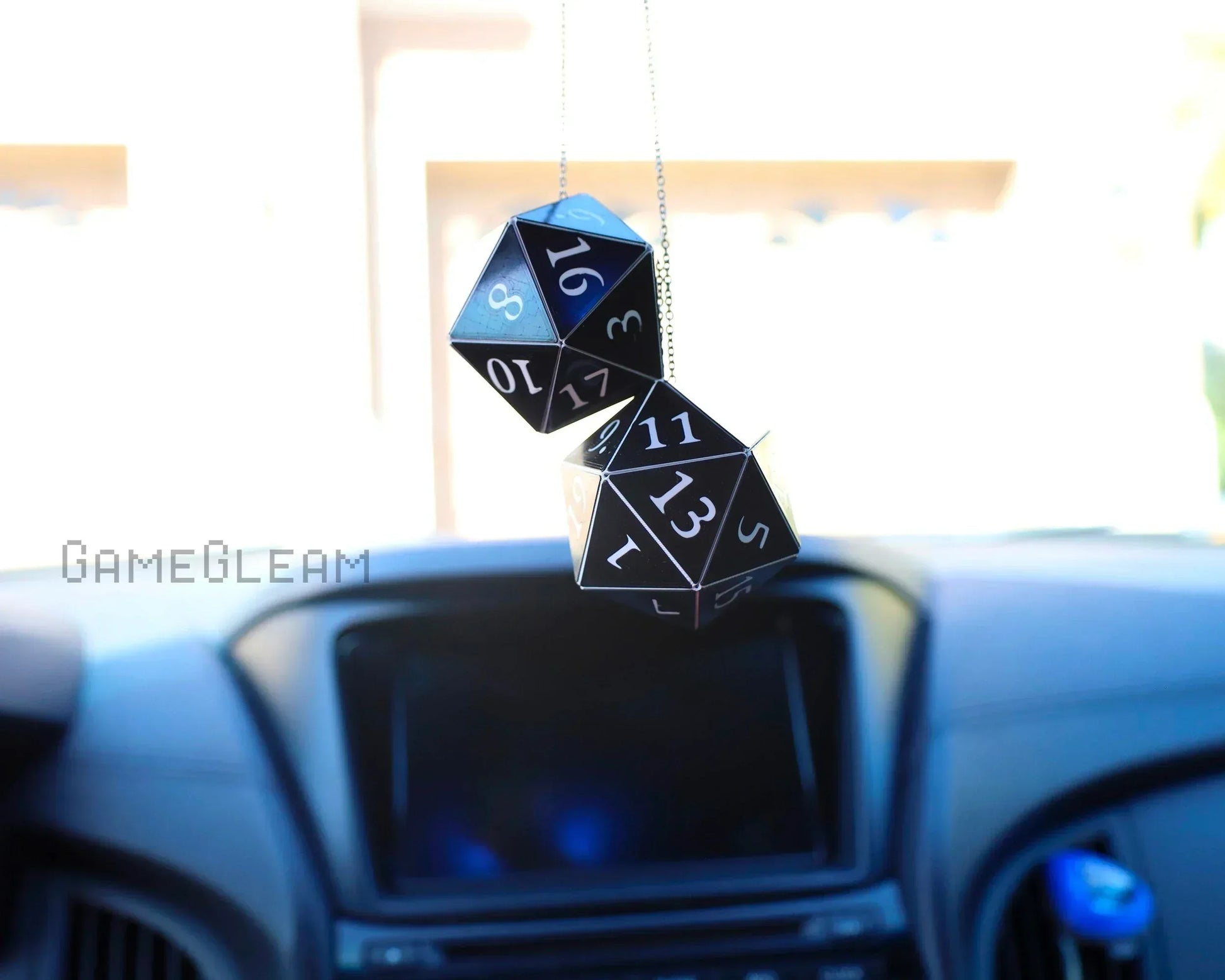 Black twenty-sided dice car charm hanging from rearview mirror in a vehicle interior