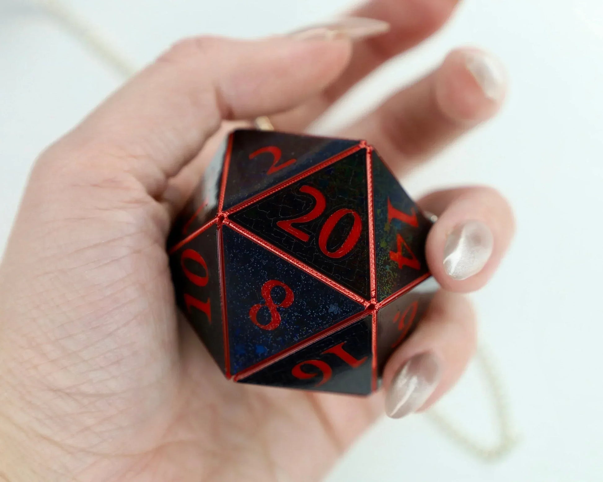 Hand holding a large dark blue twenty-sided dice with red numbers for tabletop gaming