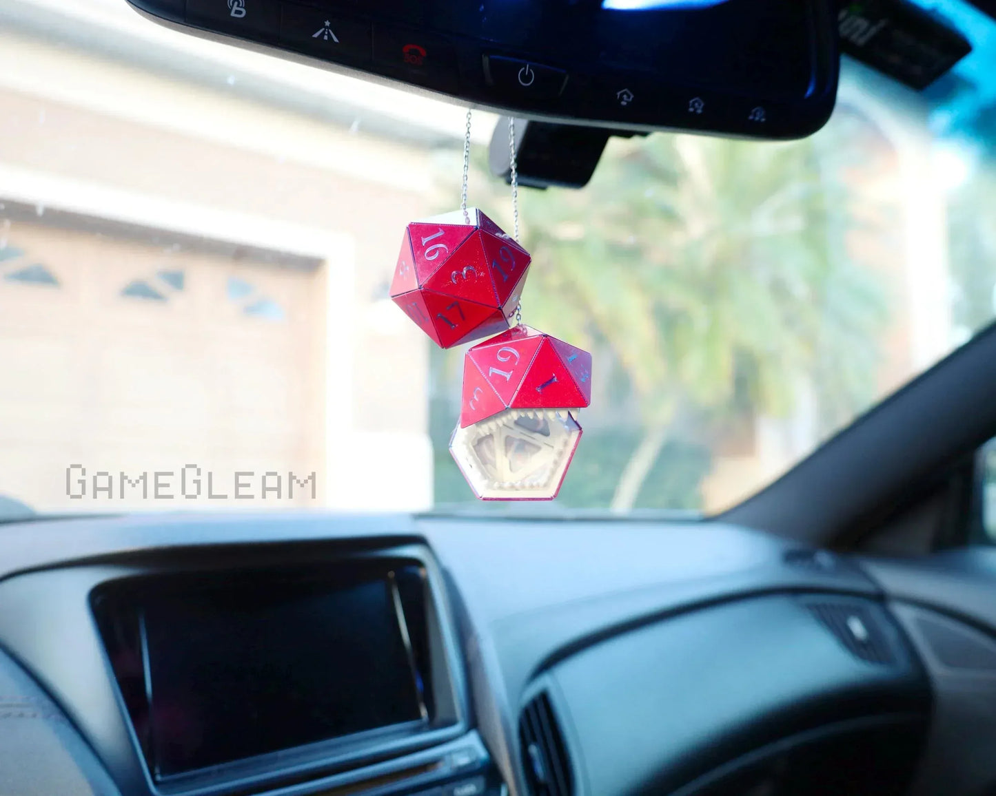 Red and clear geometric dice car charms hanging from a rearview mirror in a car interior.