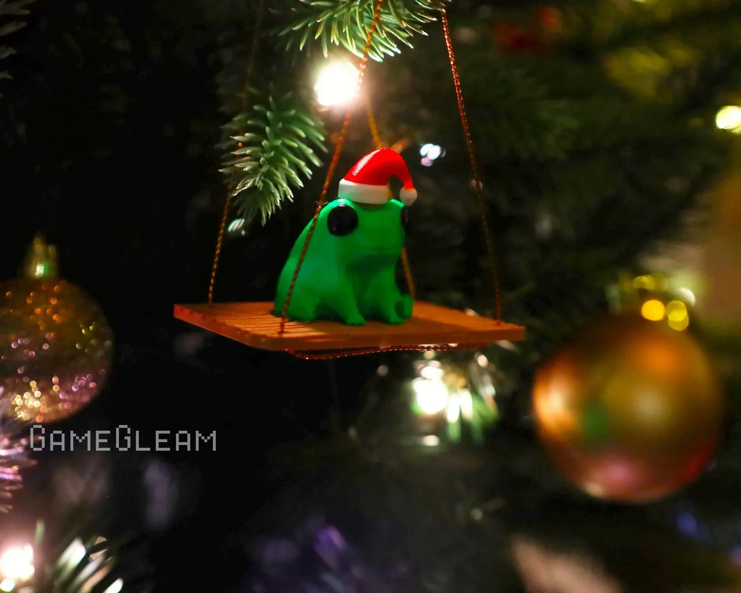 Handmade green frog ornament with Santa hat on a swing, hanging on a Christmas tree.
