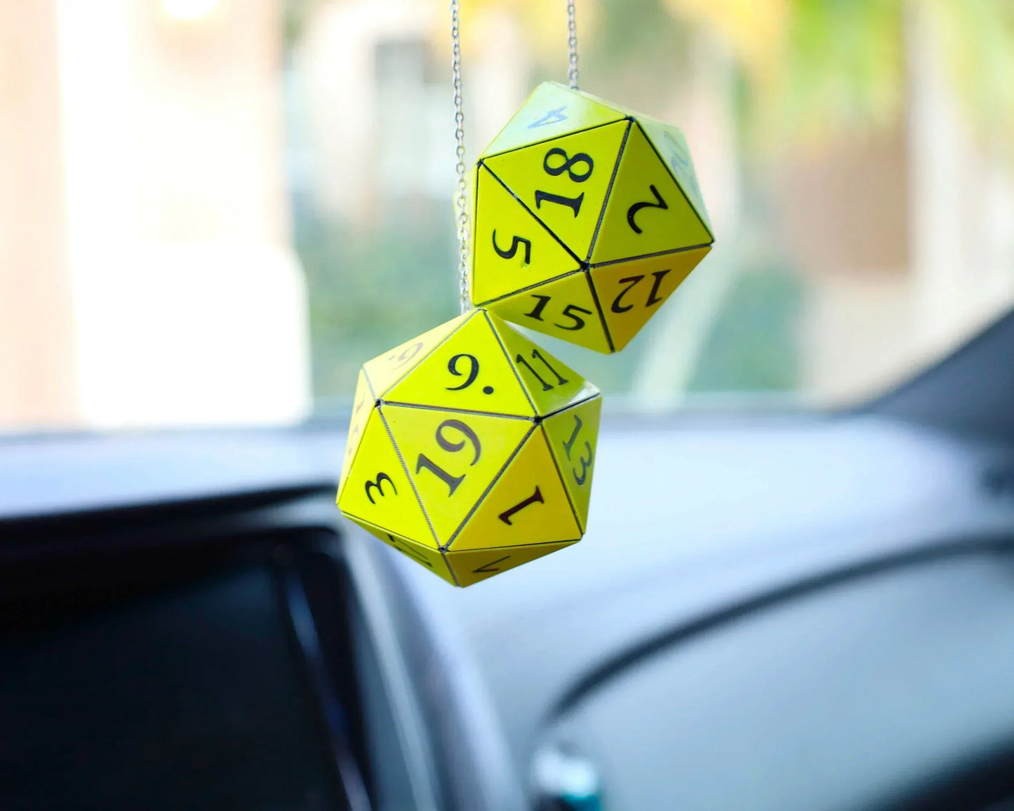 Yellow twenty-sided dice car charm hanging from rearview mirror in a vehicle interior