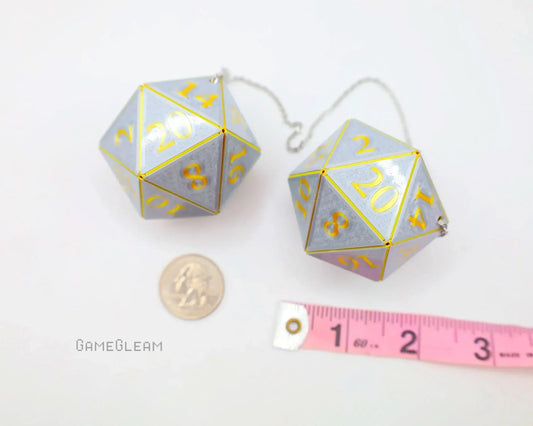 Pair of large silver 20-sided dice charms with yellow numbers, next to a ruler and coin