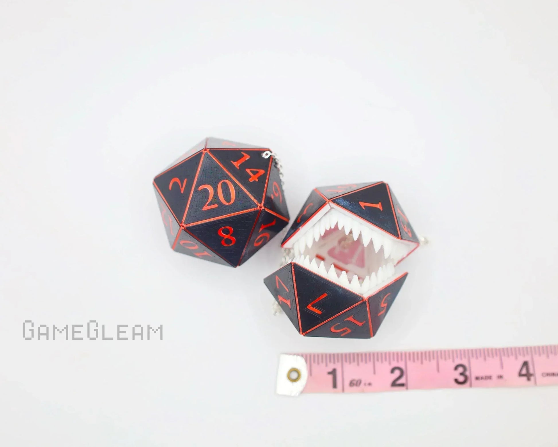 Handmade black and red twenty-sided dice charms, one with open jaws, beside a pink measuring tape