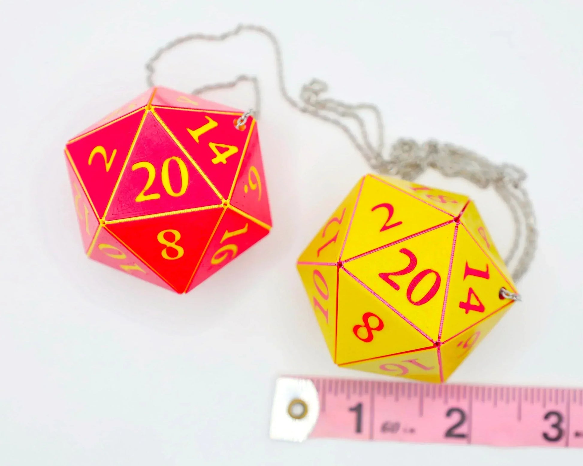 Two large, colorful twenty-sided dice car charms with chains, shown next to a measuring tape.