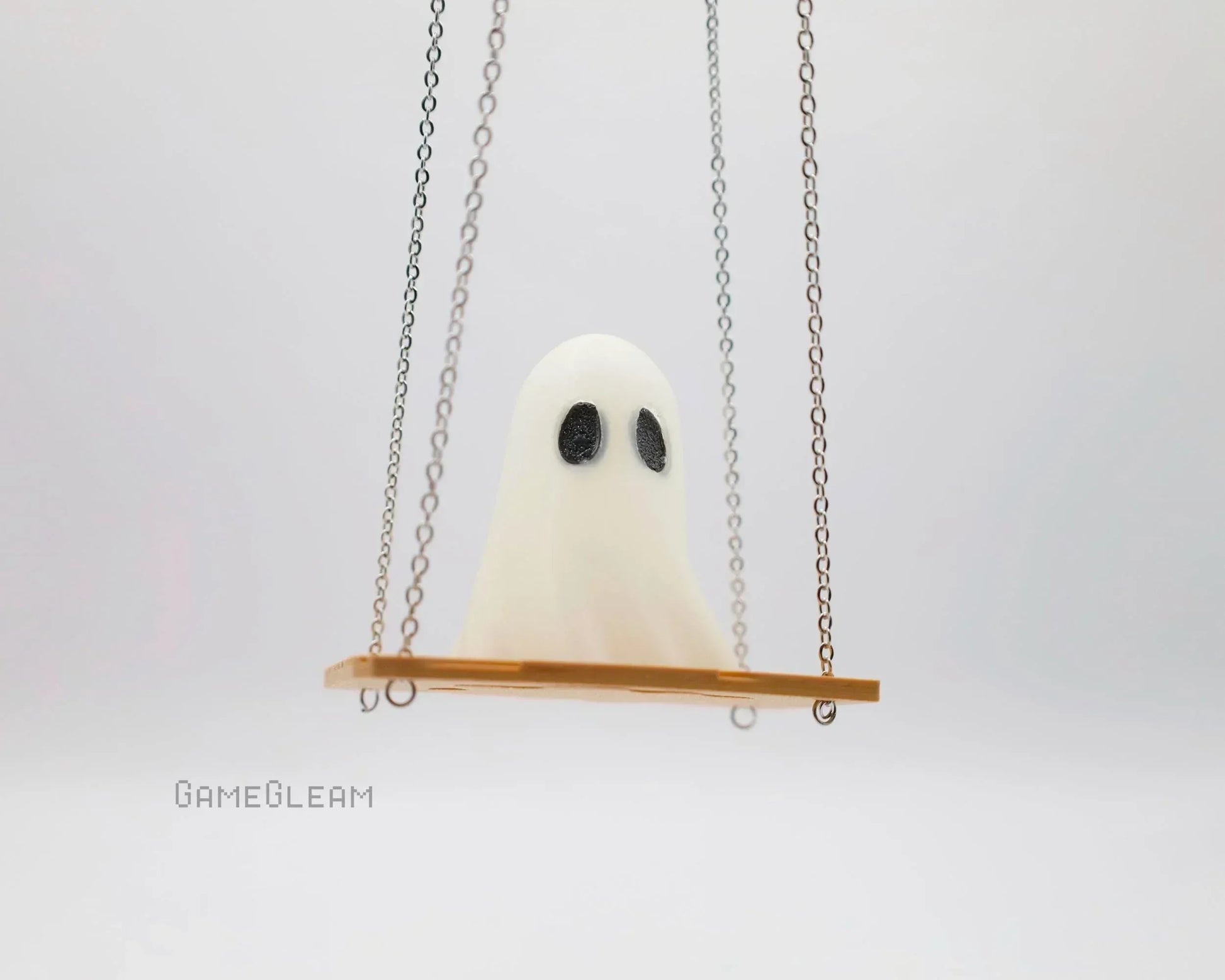 Handmade white ghost figurine with black eyes sitting on a miniature swing with metal chains