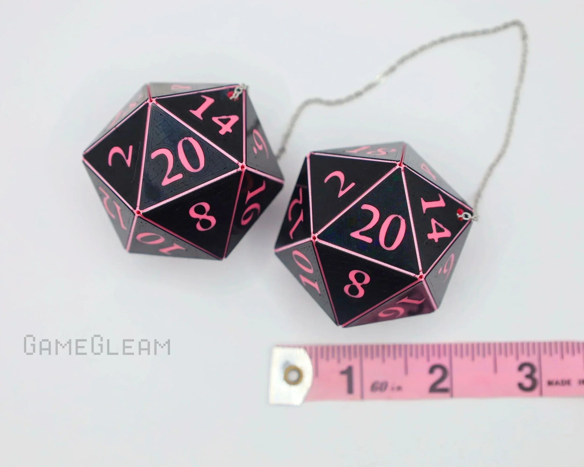 Pair of black 20-sided dice car charms with pink numbers and measuring tape for scale.