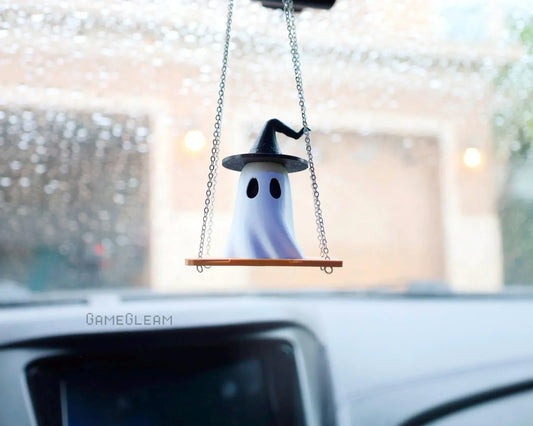 Handmade ghost charm with witch hat on swing, hanging from car mirror, rainy windshield background