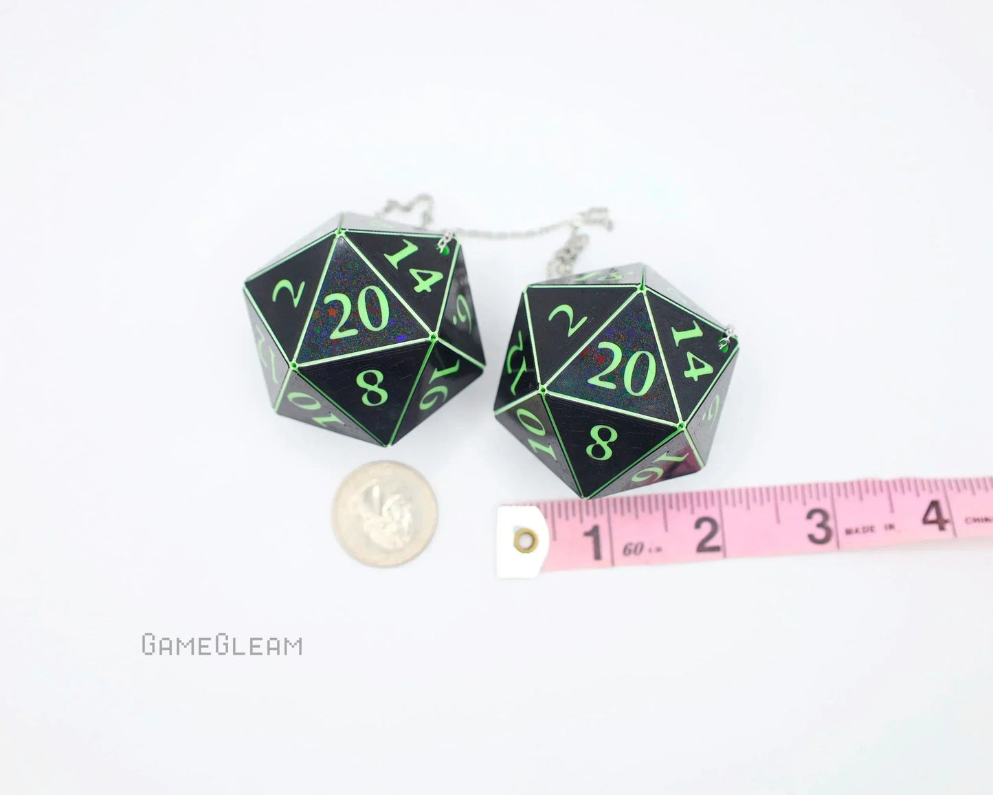 Pair of large black 20-sided dice charms with green numbers, next to a coin and measuring tape