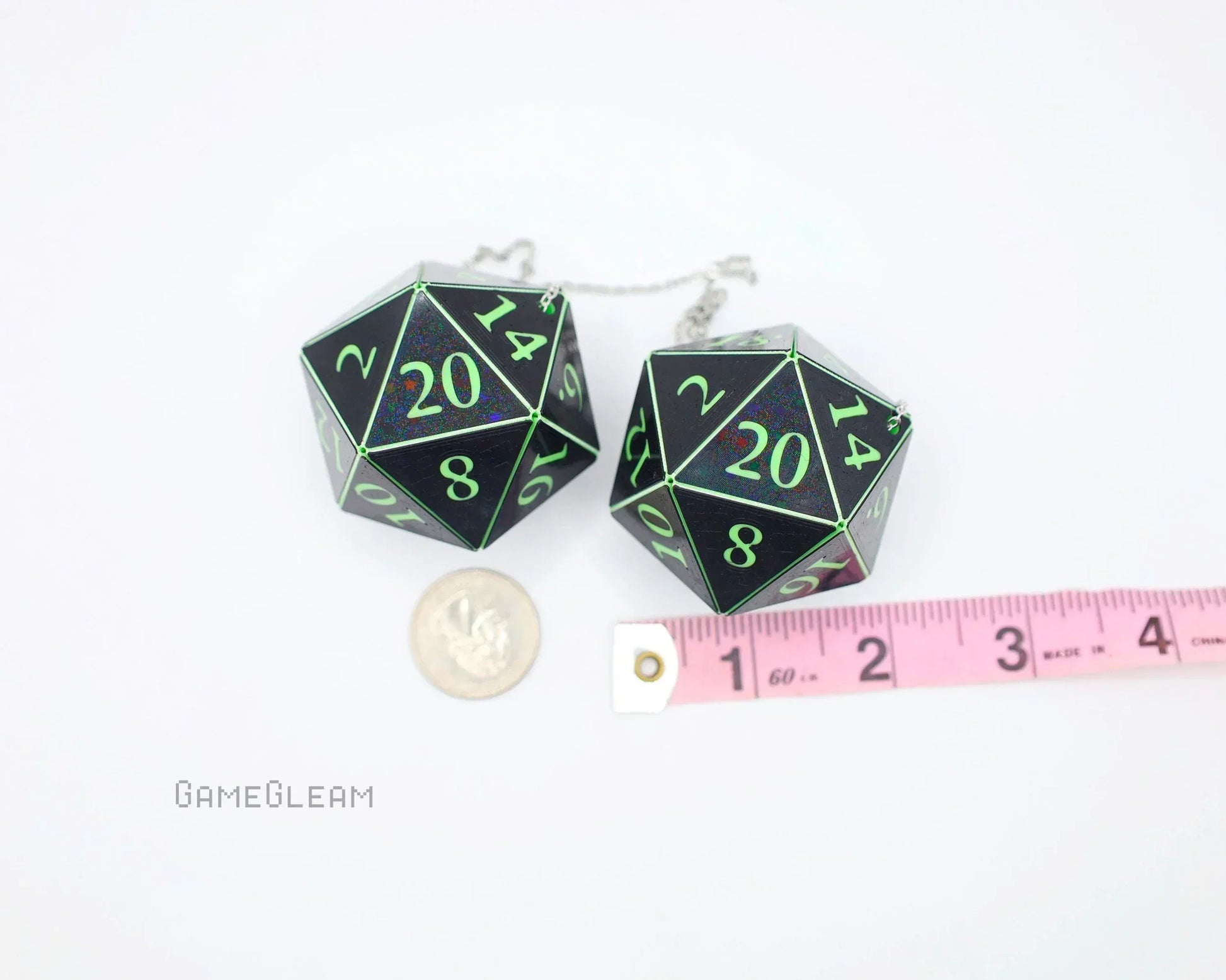 Pair of large black 20-sided dice charms with green numbers, next to a coin and measuring tape