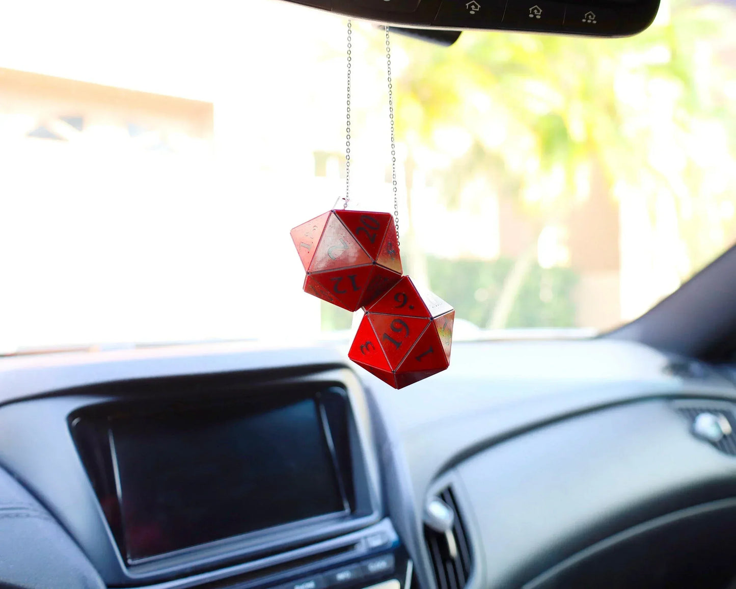 Red twenty-sided dice car mirror charm for tabletop RPG fans inside a modern vehicle.