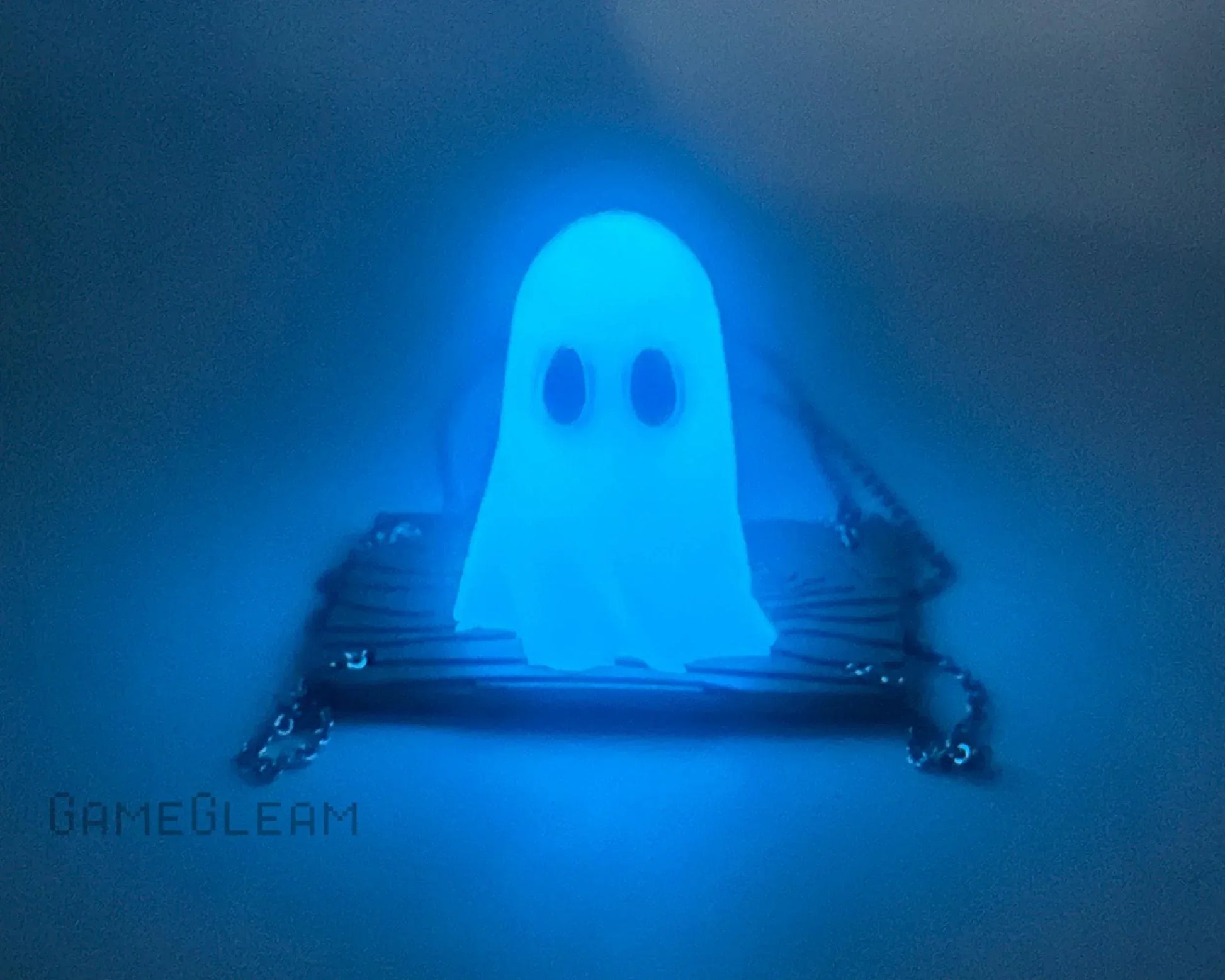 Glow-in-the-dark ghost pendant with chain on a dark background, blue LED lighting effect