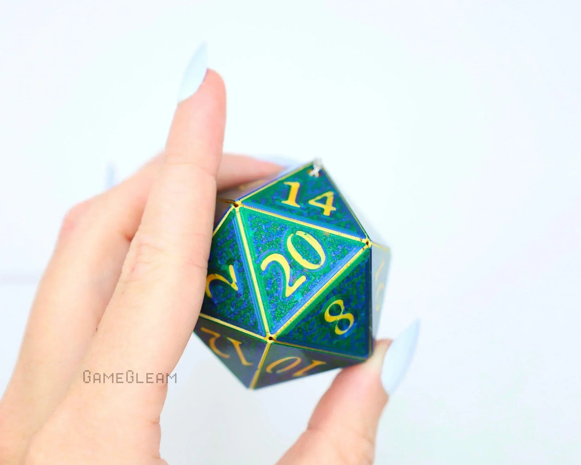 Hand holding a large holographic green-blue twenty-sided dice with gold numbers for tabletop gaming.
