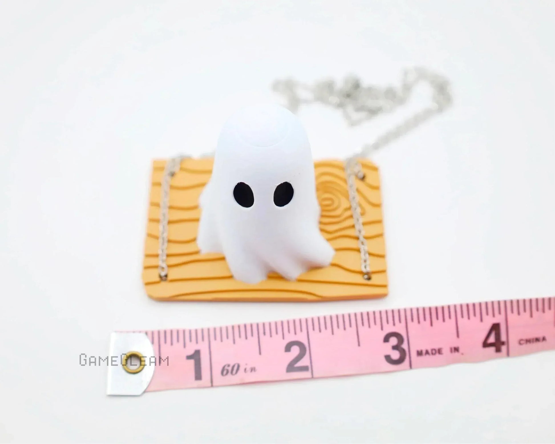 Cute ghost car charm with wood-patterned base on chain, shown with a measuring tape.