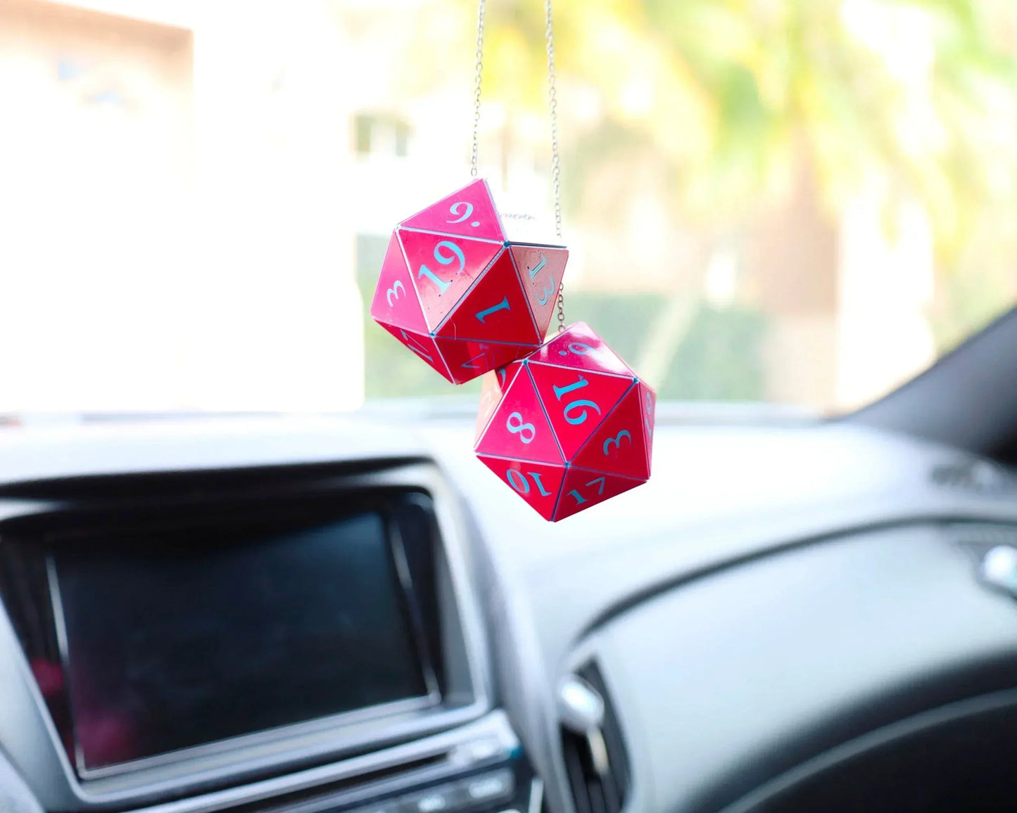 Red twenty-sided dice car charm hanging from rearview mirror in a car interior